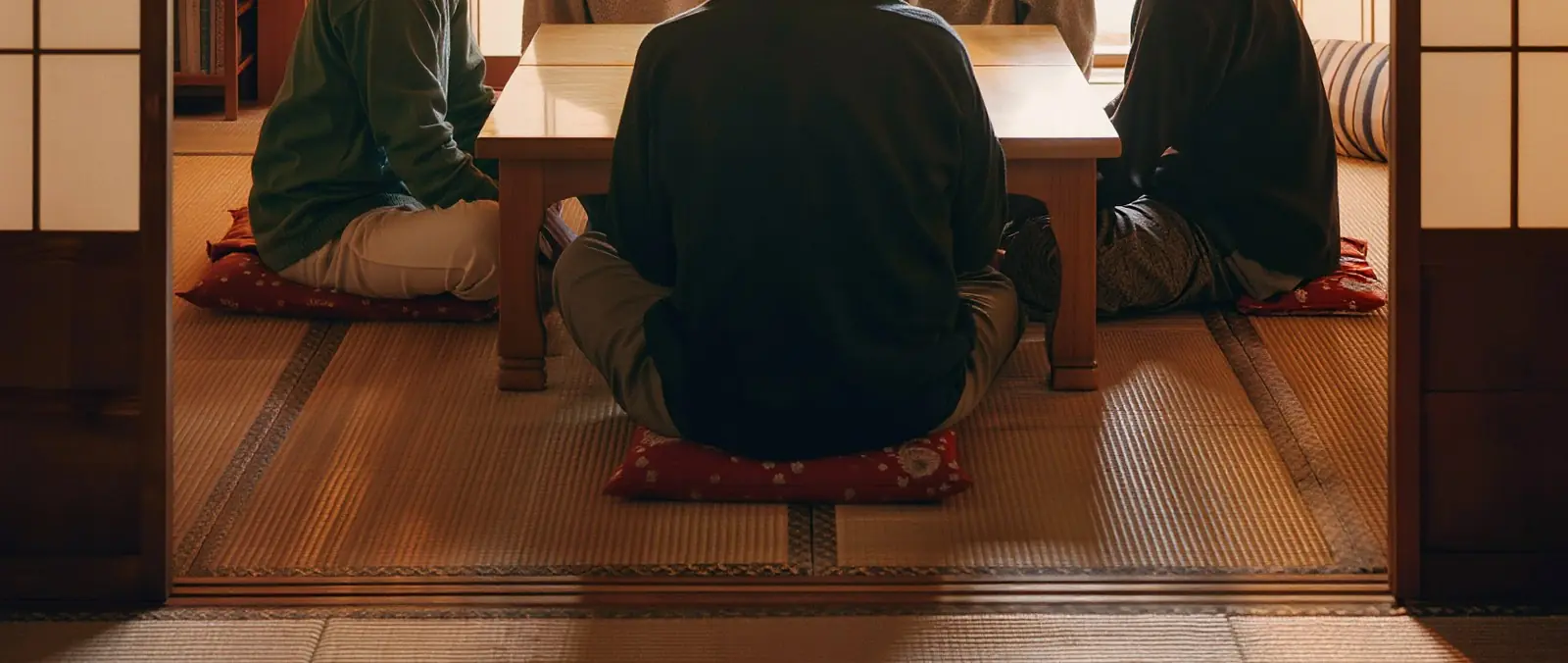 夕方の和室で、低い机を囲んで話す人たちの後ろ姿(イメージ)